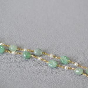 Detail of handmade necklace with green stone beads and pearls on textured fabric