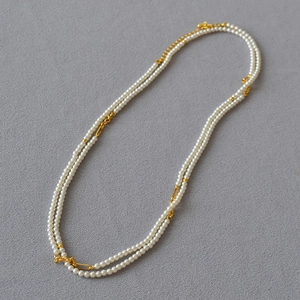 Detail of layered gold chain necklace featuring polished white pearls on grey background