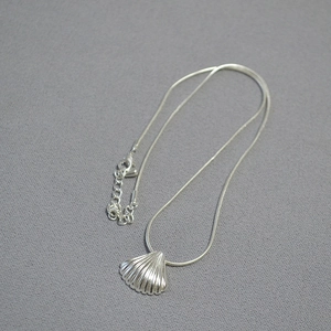 Detail of silver shell pendant necklace with snake chain on dark textured background
