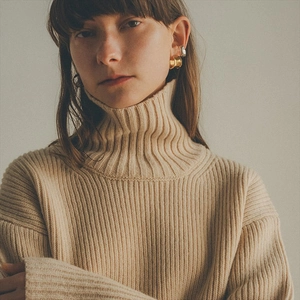 Close-up of irregular C-shaped gold and silver earrings on a model in knitwear