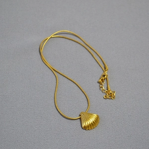 Retro gold shell pendant necklace with thin snake chain on a grey textured background