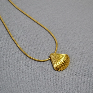 Detailed close-up of a gold shell pendant on a fine snake chain with vertical texture