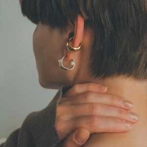 Close-up of golden ear cuff and irregular silver earring on model's ear in minimalist style