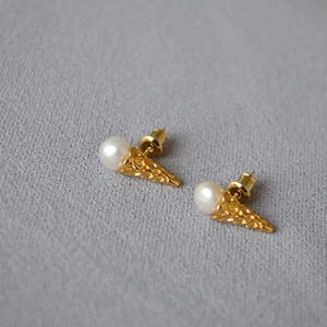 Detailed close-up of gold cone earrings featuring waffle texture and white freshwater pearls