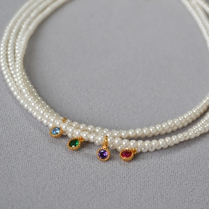 Detail of multi-layer pearl necklace with colorful gemstone pendants in gold settings