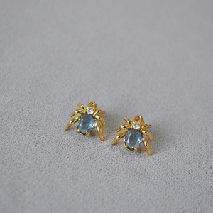 Spider stud earrings with deep blue oval gemstone and gold plated legs in macro view