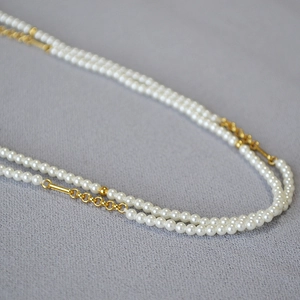 French style double-layer pearl necklace with gold chain and metal accents on grey fabric