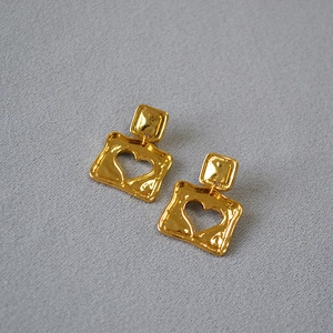 Macro shot of gold square earrings with heart cutout and hammered texture surface
