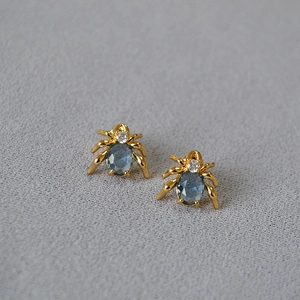 Macro shot of gold spider earrings with oval blue-grey gemstone and gothic metal design
