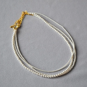 Detail einer mehrlagigen weißen Perlenkette mit goldenem Karabinerverschluss auf Stoff