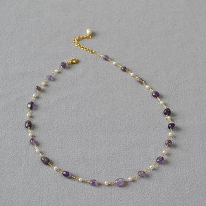 Handmade necklace with purple amethyst stones and pearls on a light grey fabric surface
