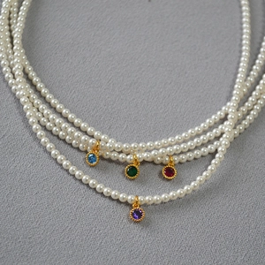 Detail of layered pearl necklace with colorful gemstone pendants on textured grey fabric