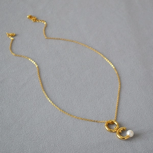 Détail du collier à pendentif double anneau doré avec perle et fermoir mousqueton