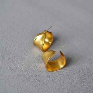 Close-up of golden irregular C-shaped earrings with a matte brushed finish on grey fabric