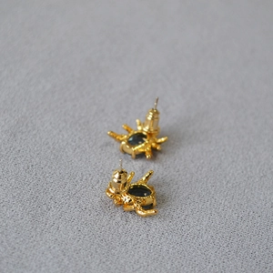 Macro detail of golden spider stud earrings featuring deep blue oval gemstones