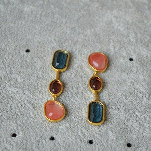 Close-up of asymmetric gold earrings with vibrant blue, brown and pink crystal stones