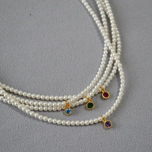 Elegant triple-layer pearl necklace featuring colorful gemstone charms in gold settings