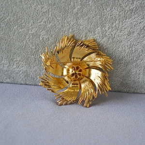 Macro detail of vintage gold twist pin with textured petals and secure rotary clasp