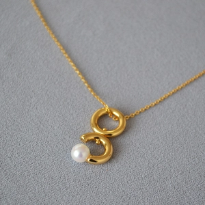 Gros plan détaillé d'un pendentif double boucle dorée avec perle sur chaîne fine