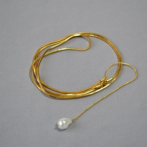 Détail d'un collier chaîne serpent dorée avec pendentif perle baroque sur tissu gris