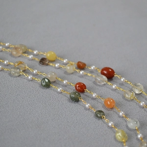 Macro detail of natural stone beads and pearls on a long layered gold necklace chain
