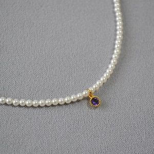 Detail of high-gloss white pearl necklace with a round purple zircon pendant in gold plating