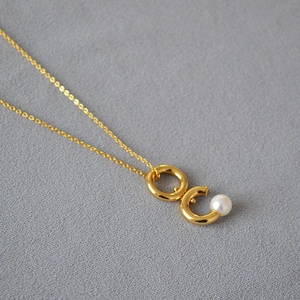 Gros plan du pendentif doré à double anneau avec perle sur une fine chaîne dorée