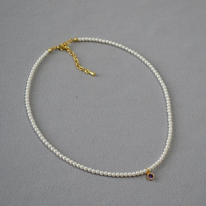 Detail of elegant pearl necklace with round purple gemstone pendant in golden setting