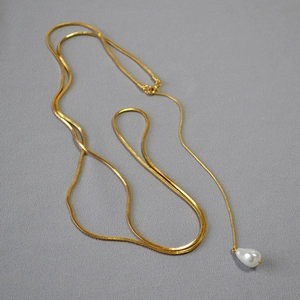 Détail d'un collier chaîne serpent dorée avec un pendentif en perle blanche en goutte