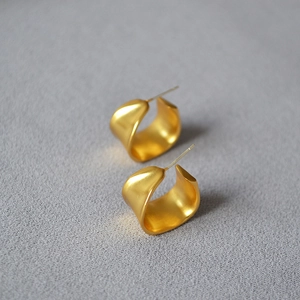 Macro detail of irregular C-shaped gold-plated brass earrings with a textured matte finish