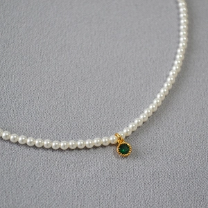 Close-up of pearl necklace featuring a green round gemstone pendant in a gold bezel