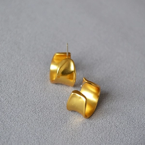 Detailed macro view of wide C-shape matte gold earrings with fine brushed metal texture