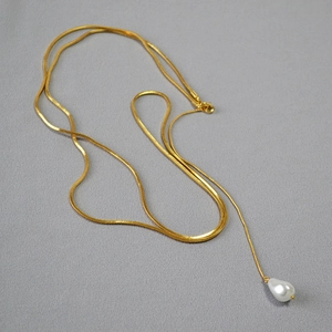Détail de la chaîne serpent dorée avec pendentif en perle blanche en forme de goutte