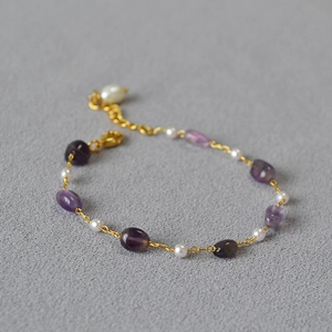 Detail of beaded gold chain necklace with purple stones and pearls on grey surface