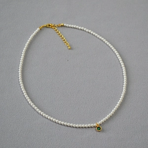 Close-up of pearl necklace with a round green gemstone pendant and golden lobster clasp