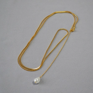 Détail d'une chaîne serpent dorée ornée d'un pendentif en perle blanche en goutte