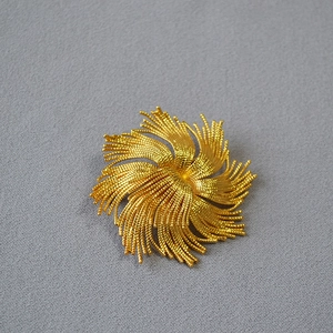 Detailed close-up of a vintage golden twist brooch with firework texture and beadwork