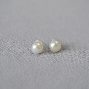 Macro shot of 8mm freshwater pearl earrings with 925 silver pins on gray fabric texture