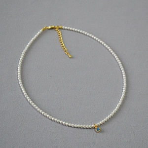 Detail of pearl necklace featuring a blue zircon pendant and golden lobster clasp