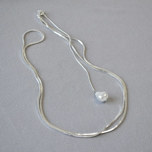 Détail du collier chaîne serpent argentée avec perle en forme de goutte sur fond texturé