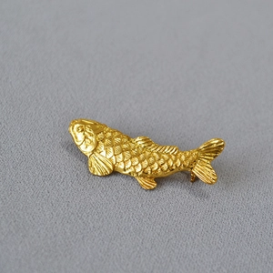 Close-up of golden koi fish brooch with detailed scales on grey textured fabric