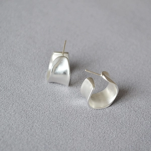 Detailed close-up of silver irregular wave earrings with a matte brushed metallic finish