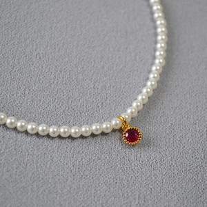 Close-up of elegant pearl necklace featuring a round red gemstone pendant with gold trim