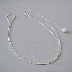 Détail d'un collier chaîne serpent argenté élégant avec pendentif perle blanche sur fond gris