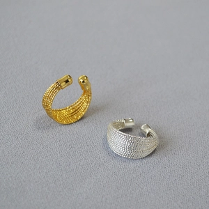 Détail de boucles d'oreilles ear cuffs tressées en or et argent sur tissu texturé
