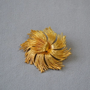 Detailed top view of a gold-plated vintage sunburst brooch with textured twisted metal wires