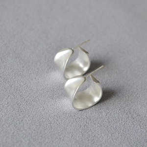 Macro shot of minimalist silver irregular C-shape earrings with a brushed matte finish