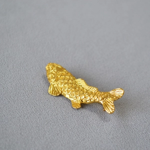 Close-up of golden koi fish brooch with detailed scales on textured grey background