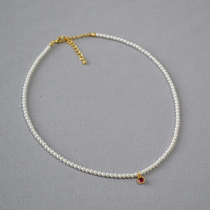 Detailed shot of small round pearls with a red gemstone pendant and gold clasp