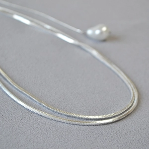 Vue détaillée d'un collier chaîne serpent argenté avec un pendentif perle blanche en goutte